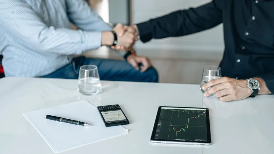 Business partners shaking hands across a table with financial charts