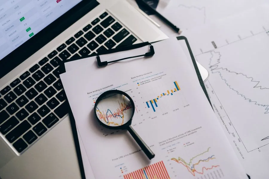 Investment charts examined with a magnifying glass beside a laptop